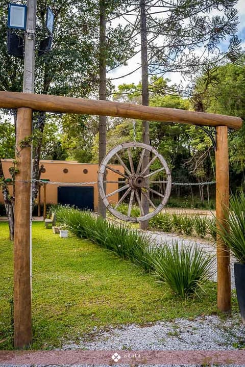 Portal rústico de eucalipto com roda de carroça e araucárias ao fundo